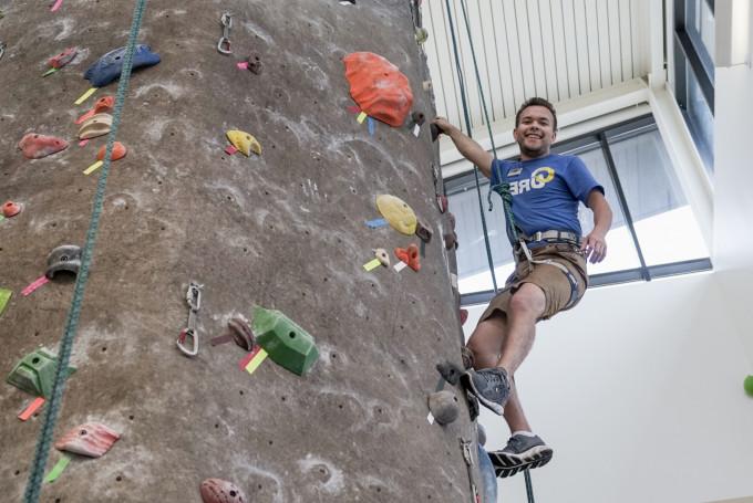 student smiling for the camera while climbing the rock wall